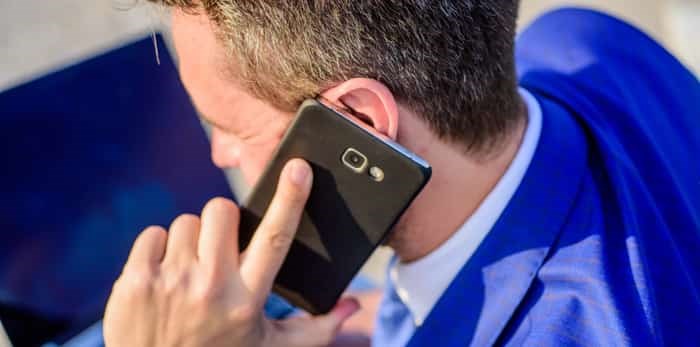  Businessman holds smartphone near ear close up / Shutterstock