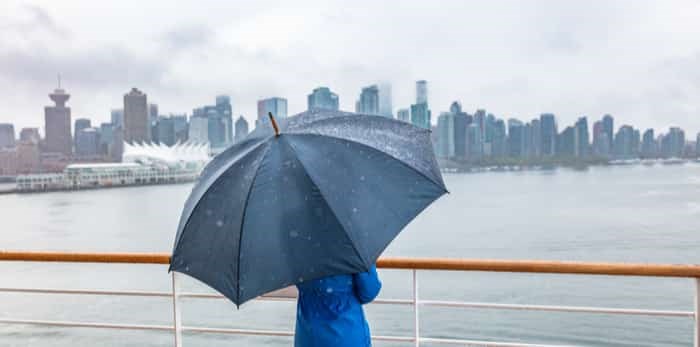  Woman leaving port watching city skyline of Vancouver under the rain with umbrella / Shutterstock