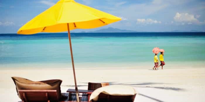  Two women pass by the yellow beach umbrella / Shutterstock