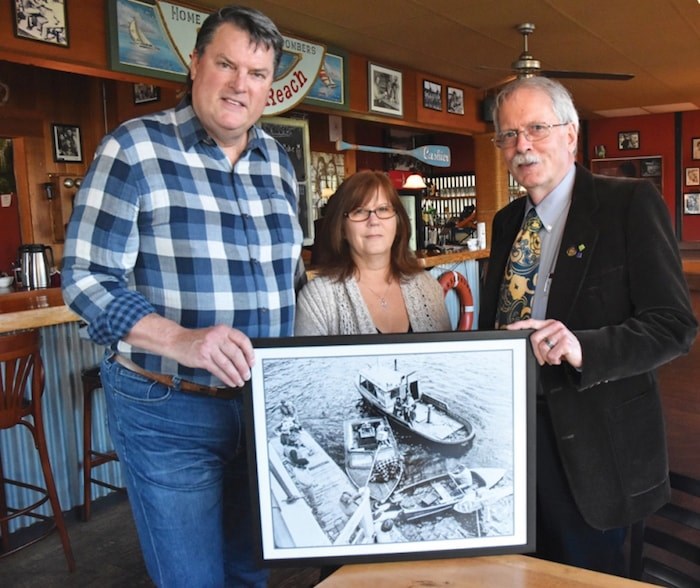  John Wade (left) presents a photograph featuring his grandfather, actor Frank Wade, who played Colonel Spranklin in The Beachcombers. Next to him is Molly’s Reach owner Diane Twohig and Gibsons Coun. David Croal, who worked as an art director on the show. Colonel Spranklin appears in the rowboat in the bottom right of the photo. Photo by Sophie Woodrooffe/Coast Reporter