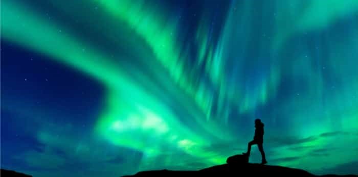  Aurora borealis with silhouette standing man on the mountain / Shutterstock