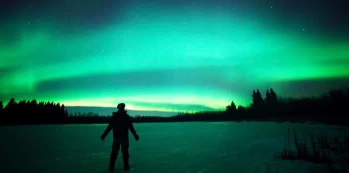  The ghostly colors of the aurora borealis captured above an unidentified person standing on a frozen lake in northern Canada / Shutterstock