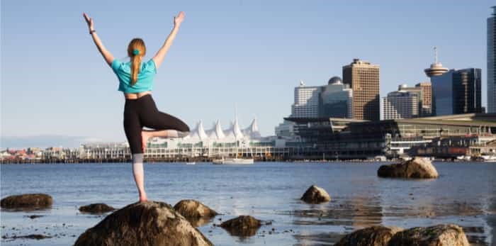  Woman practicing yoga in Stanley Park with city skyline in the background / Shutterstock