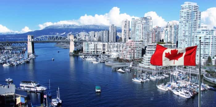  Canadian flag in front of view of False Creek and the Burrard street bridge in Vancouver, Canada. / Shutterstock