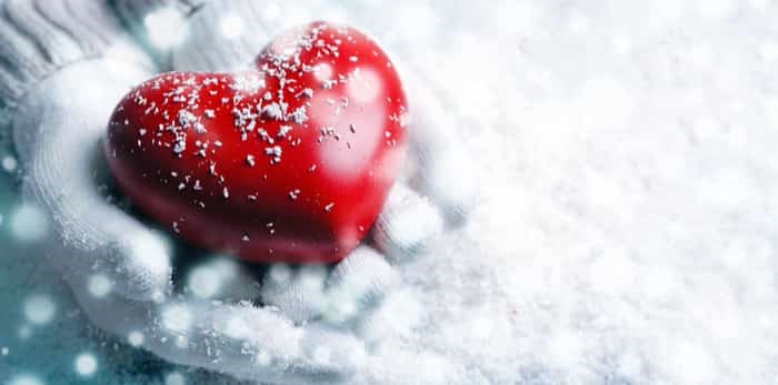  Hands in warm white gloves holding red heart on snowy background / Shutterstock