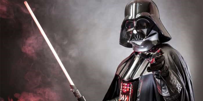  SAN BENEDETTO DEL TRONTO, ITALY. MAY 16, 2015. Portrait of Darth Vader costume replica with grab hand and sword . Darth Vader is a fictional character of Star Wars saga. Red grazing light and smoke / Shutterstock