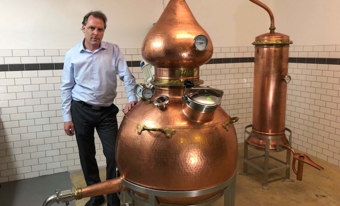  Paul Doroshenko standing in front of his hand-hammered copper still from Spain in his Richmond office. Photo courtesy Paul Doroshenko.