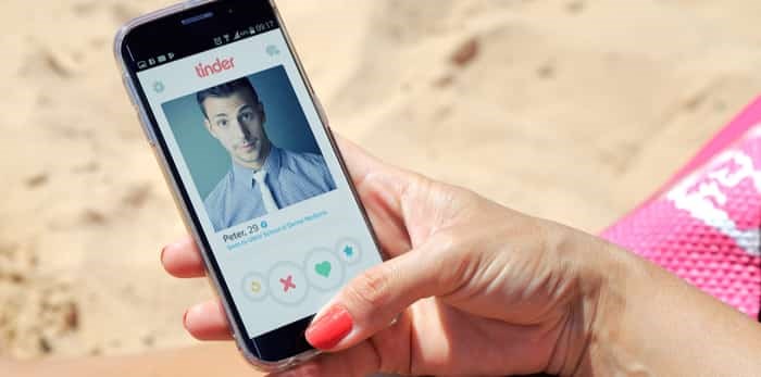  ROSARIO, ARGENTINA - JANUARY 14, 2017: Woman on the beach with a cell phone in her hands. On the screen you can see the Tinder application with a man profile open / Shutterstock