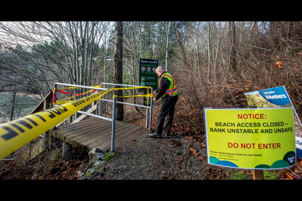 Saanich Parks worker Mike Goldsworthy puts up signs and warning tape at the entrance to beach stairs in Arbutus Cove Park in Saanich on Thursday, Dec. 23, 2021. DARREN STONE, TIMES COLONIST