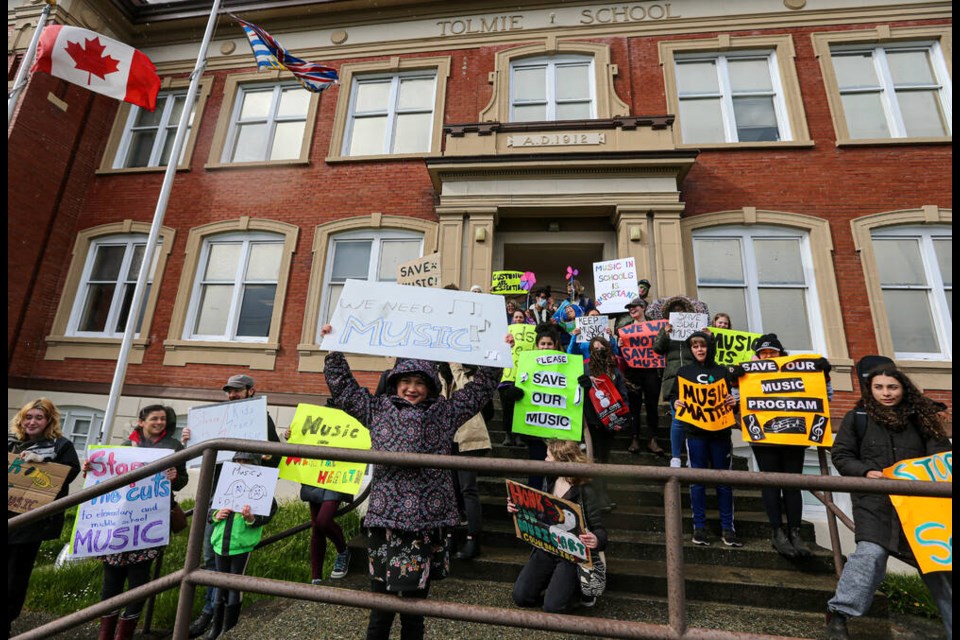 Matilda Geater, 9, from Oaklands Elementary, centre left, holds a sign high, as students and parents protest proposed cuts to music programs, custodians and counsellors in front of the Greater Victoria School District offices on Boleskine Road on Monday. ADRIAN LAM, TIMES COLONIST 