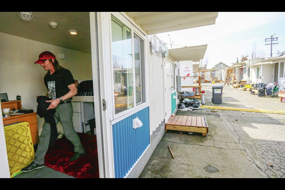 Resident Jay Leggatt tidies up his 100-square-foot micro-home, which has a bed, small dresser, wardrobe and small refrigerator  but no stove. There are communal washroom facilities, as well as a place where he can heat up food. ADRIAN LAM, TIMES COLONIST 