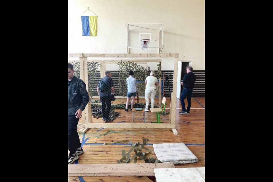 Volunteer videographer Brendan Strain, left, and Langford Mayor Stew Young, right, observe volunteers making camouflage netting in a school gymnasium. VIA BOB BECKETT 