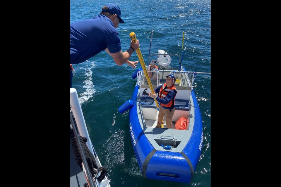 A member of the U.S. Coast Guard passes a long metal pipe to a volunteer from the Whale Museum's Soundwatch team. The pipes are being placed in the water and banged with a steel hammer in an effort to divert whales from the area where a vessel sank on Saturday, Aug. 13, 2022. U.S. COAST GUARD