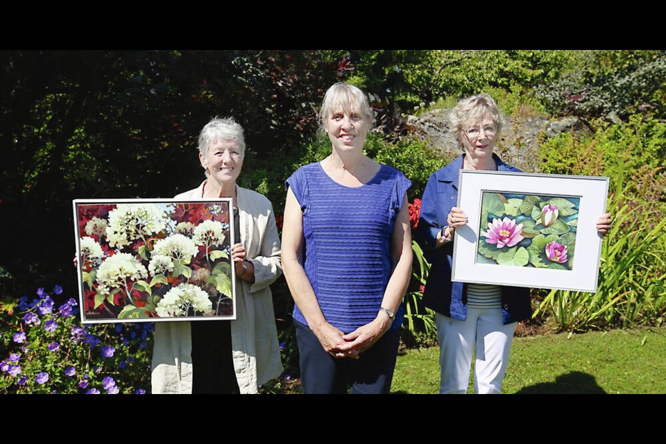 Abkhazi Garden site manager Cherie Miltimore, centre, with artists Christine Gollner, left, holding Limelight Hydrangea, and Myra Baynton, holding Lilypad Closeup. An art show fundraiser at the garden begins Monday and features paintings and sketches created by 15 local artists and inspired by the garden. Proceeds are to be divided between the artists and The Land Conservancy, which purchased the Gonzales-area site in 2000 to keep it from being developed. ADRIAN LAM, TIMES COLONIST 