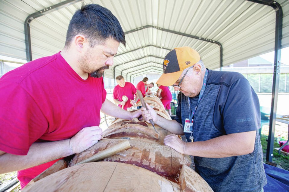 Artist Aubrey LaFortune, right, guides Roger Der in carving a section of a totem pole at the Vancouver Island Regional Correctional Centre. ADRIAN LAM, TIMES COLONIST.  Aug. 17, 2022