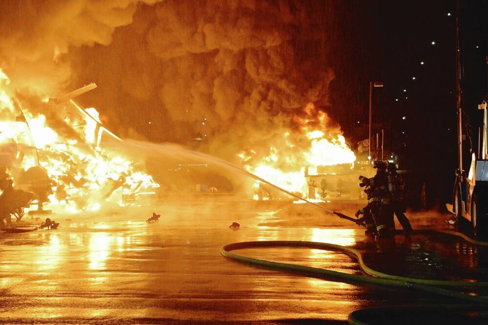 In this image provided by John Odegard, firefighters in Seattle douse flames at a marina on Lake Union, near the city's University District, early on Wednesday, March 22, 2023. The fire burned 30 boats on a dry-rack storage facility, and a man found hiding in one vessel was arrested for investigation of arson, authorities said. (John Odegard via AP)