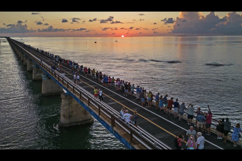 In this aerial photo provided by the Florida Keys News Bureau, attendees watch and toast the sunset at a Florida Keys bicentennial celebration, Friday, May 19, 2023, on the restored Old Seven Mile Bridge in Marathon, Fla. The sunset gathering was among a series of Keys events being staged to mark the 200th anniversary, on July 3, of the Florida Territorial Legislatures 1823 founding of Monroe County, containing the entire island chain. The old bridge was originally part of Henry Flaglers Florida Keys Over-Sea Railroad completed in 1912, and is now closed to vehicles but open to pedestrians and bicycles. (Andy Newman/Florida Keys News Bureau via AP) 
