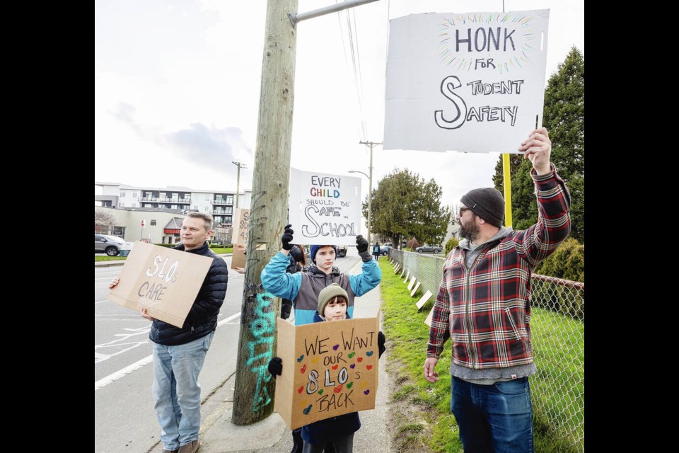 From left, Mark Jenkins, Tomas Lee, 9, Thomas Lee, 12, and Jaye Lee hold signs at a rally in front of the Greater Victoria School District office on Boleskine Road on Monday. DARREN STONE, TIMES COLONIST 