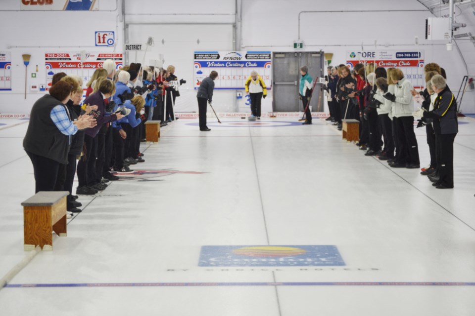 Curlers cheer and applaud as Maxine Heritage of Virden throws the ceremonial first rock during the opening ceremonies. Sweeping are Diane Elliott, left, and Shannon Kinnaird.