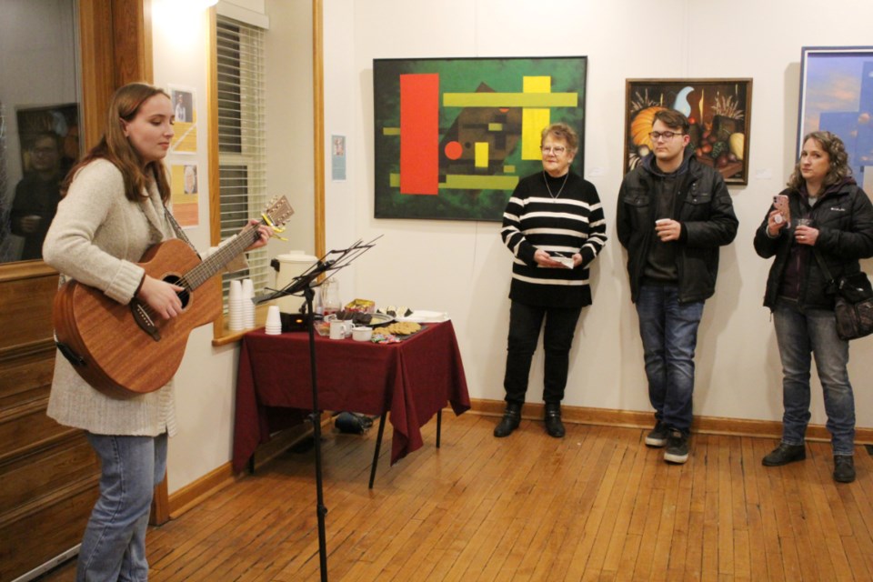 Daelyn Fefchak, back for the weekend from her first year at Brandon University as a voice major, performs Hey, Soul Sister for an audience of artists and friends. George Baker’s art is seen on the opposite wall.