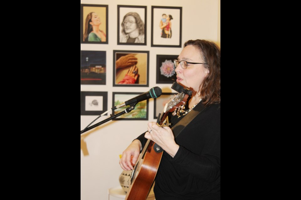 Krista Pederson plays and sings in the Station gallery to open the public reception for artist Dhairya Vaidya. His work is seen in the backdrop. 