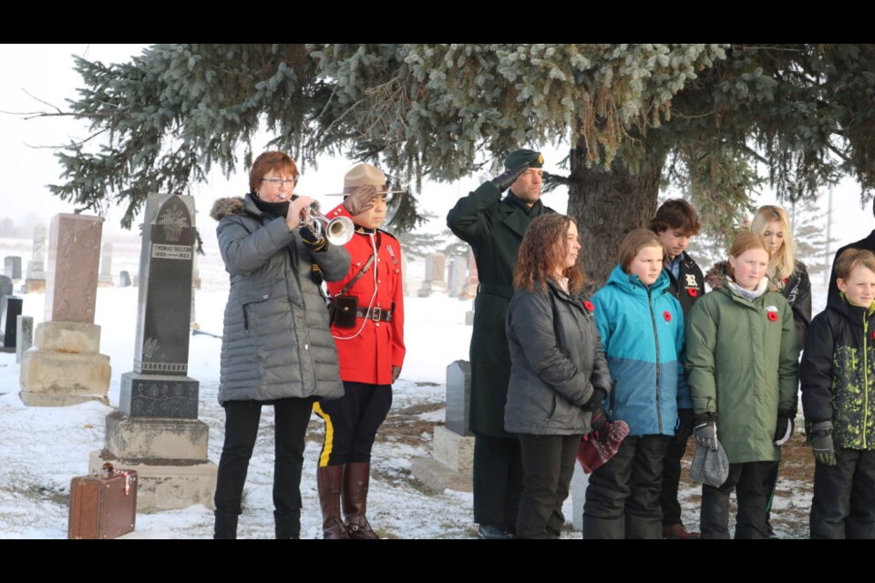 At a graveside ceremony of Remembrance, Reston music teacher Michelle Gervain plays The Last Post. Saluting are RCMP Constable Kim and Captain Derek Millard with Reston School Gr. 5 and 6 students. PHOTO/NICK TINGEY