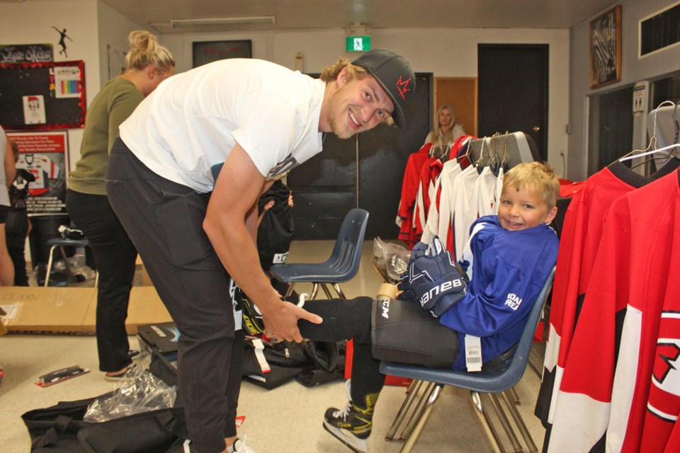 Travis Sanheim helps a youngster into hockey gear.