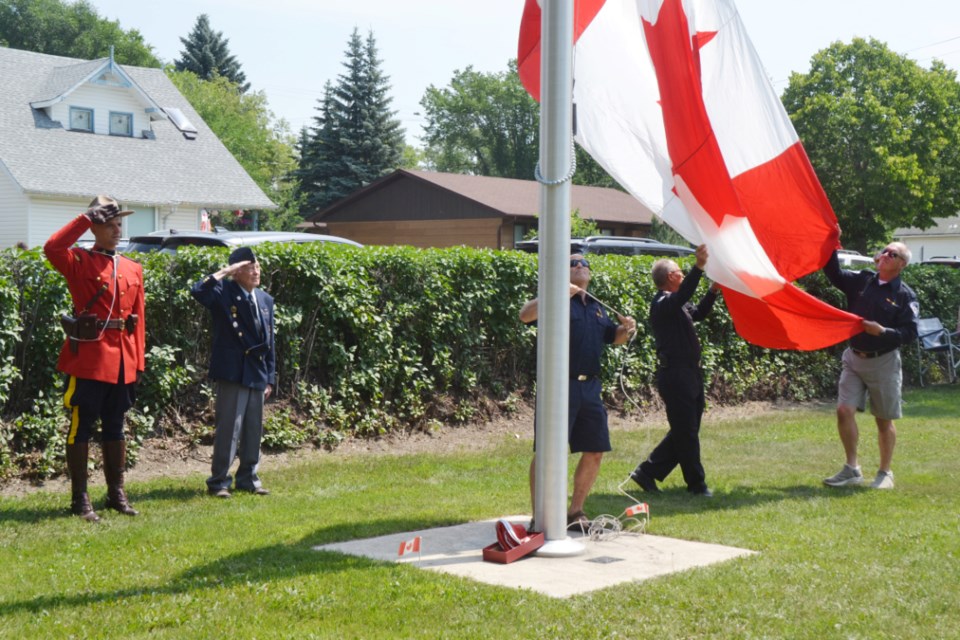 RCMP Cpl. Eduardo Giannico, left, and WW2 Veteran Cde. John Fefchak salute as the Canadian Flag is hoisted high atop the Victoria Park flag pole by three long-serving members of the Wallace District Fire Department, at right, John Davidson, Curtis Smith and Brad Yochim. 